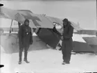 Två flygare står vid havererat militärt flygplan Aviatik nr 30.14  tillhörande Österrike-Ungern, efter kollision med flygplan Brandenburg B.1 nr 05.26 den 9 februari 1917. Vy från sidan.