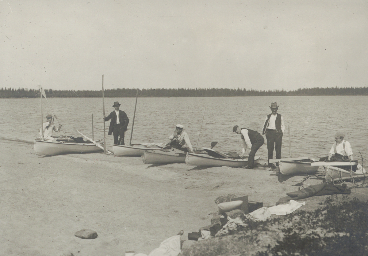 Kanotister med paddelkanoter på strand.