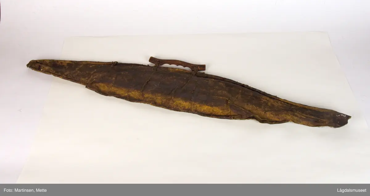 Bueveske av skinn. Pelssiden inn, sydd med sene Plass for piler og bue. Bærehåndtak av tre festet til buevesken med skinnsnorer, sydd med sene. I nederkant ca. 32 cm lang sprekk til åpning.