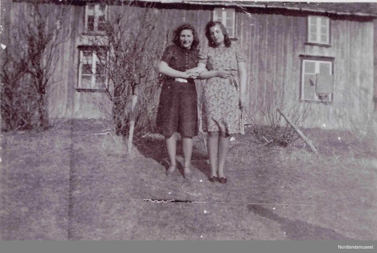 To unge kvinner. Ida Annie Elisa Martinusen, født i 1926, fra Bø og Lilly (Lilla) Falch Danielsen, født i 1927,  fra Stegen på Engeløy i Steigen. De står utenfor huset til Martin Kaspersen.