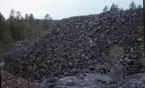 Flätsbo gruva. Stor hög av bruten sten. Skog i bakgrunden.