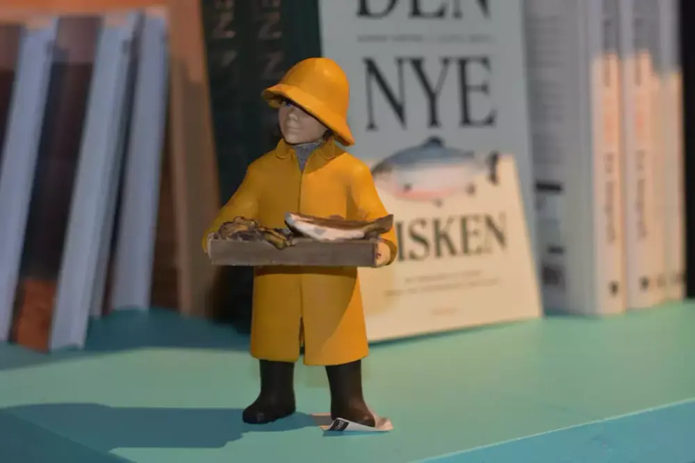 En liten figur i gult regntøy med sydvest holder en stor fisk