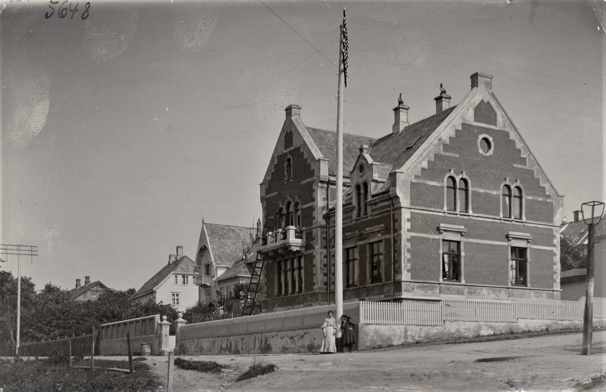Elise Karoline Knudsen og Thorval Johan Kyviks villa i Strandgata 211, Haugesund. To kvinner står under en telegrafstolpe på hjørnet av huset.