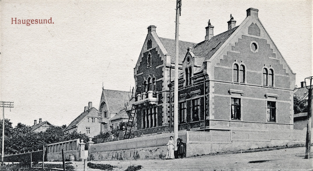 Elise Karoline Knudsen og Thorval Johan Kyviks villa i Strandgata 211, Haugesund. To kvinner står under en telegrafstolpe på hjørnet av huset.
