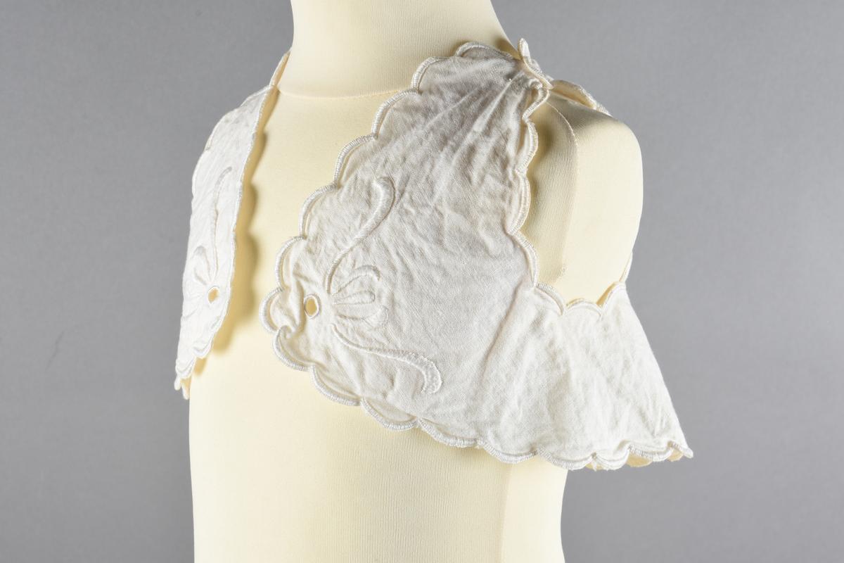 Vest til spedbarn. Bomull. Et stykke som har blitt sydd sammen for å lage ermehullene. Dekorert med broderier. Motiv av blomster.