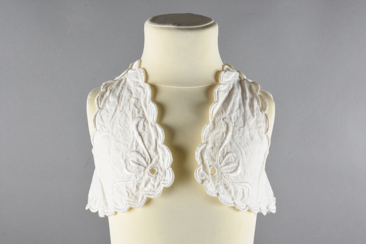 Vest til spedbarn. Bomull. Et stykke som har blitt sydd sammen for å lage ermehullene. Dekorert med broderier. Motiv av blomster.