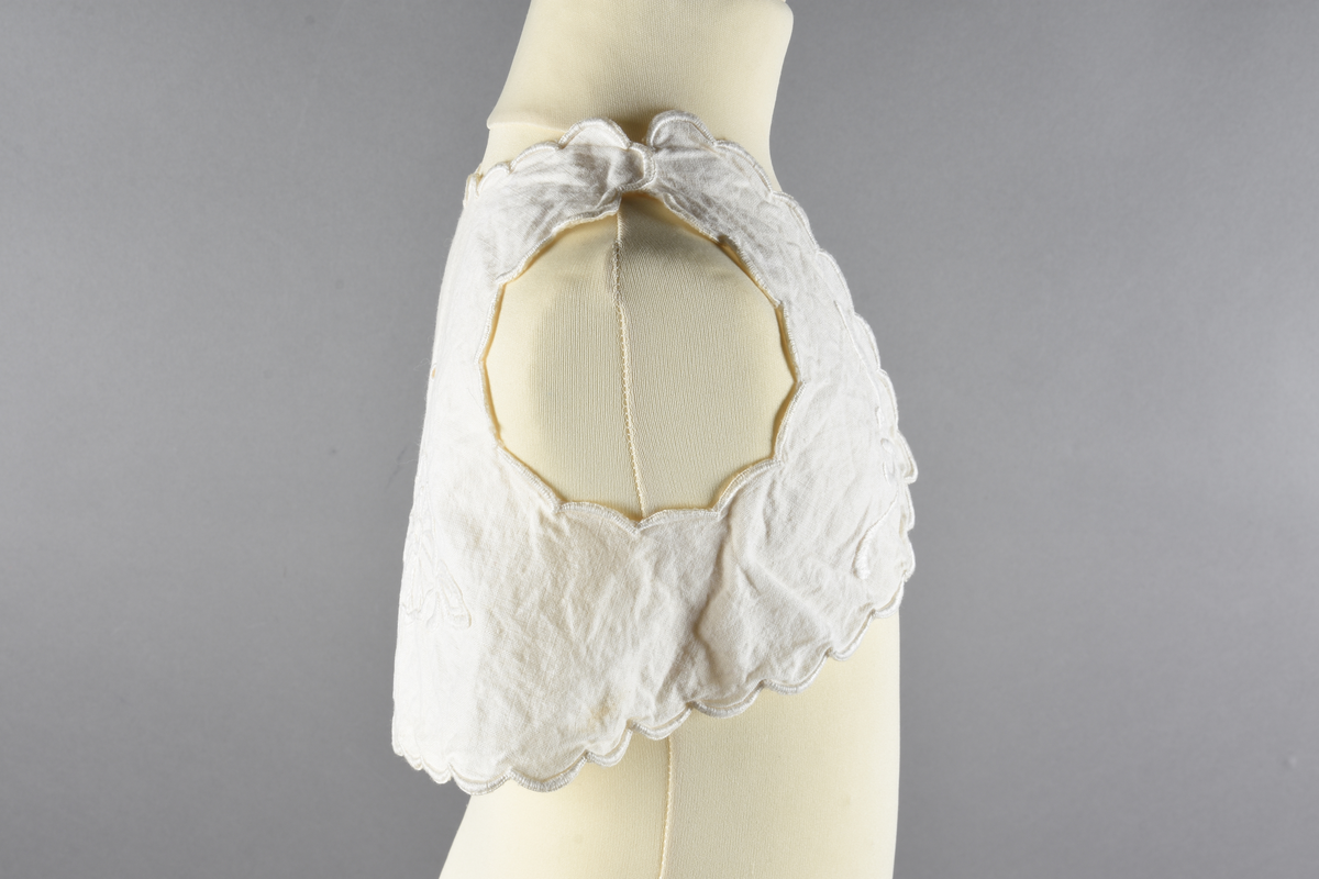 Vest til spedbarn. Bomull. Et stykke som har blitt sydd sammen for å lage ermehullene. Dekorert med broderier. Motiv av blomster.