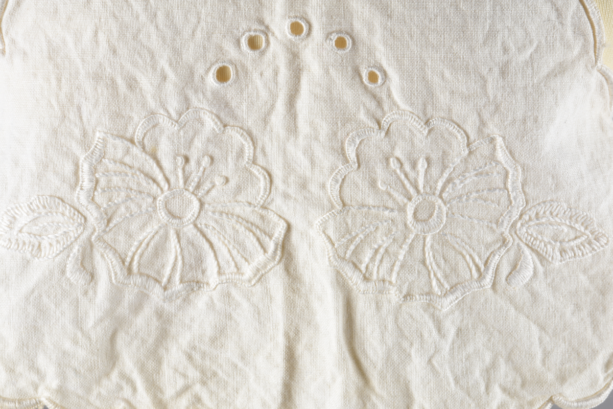 Vest til spedbarn. Bomull. Et stykke som har blitt sydd sammen for å lage ermehullene. Dekorert med broderier. Motiv av blomster.