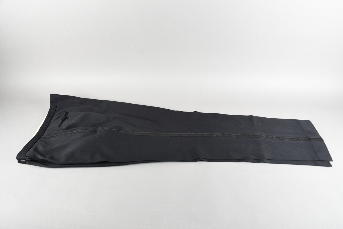 Bukse. Fire plastknapper i gylfen og to metallhemper til lukking. To baklommer med en plastknapp hver til lukking. Hvitt fôr til lommene og linning innvendig.
