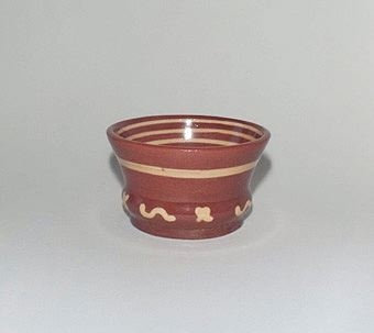 Liten glaserad rödbrun skål av lergods med gult hornmålat mönster.