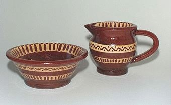Rödbrun glaserad sockerskål av lergods (tillhörande gräddkanna finns) med gult hornmålat mönster.