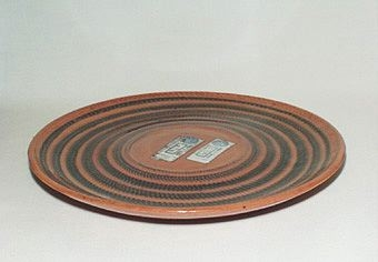 Fat i lergods. Bottenfärgen utgörs av lerans naturliga färg, ovanpå mörka ringar som hämrats. Hela fatet är glaserat.