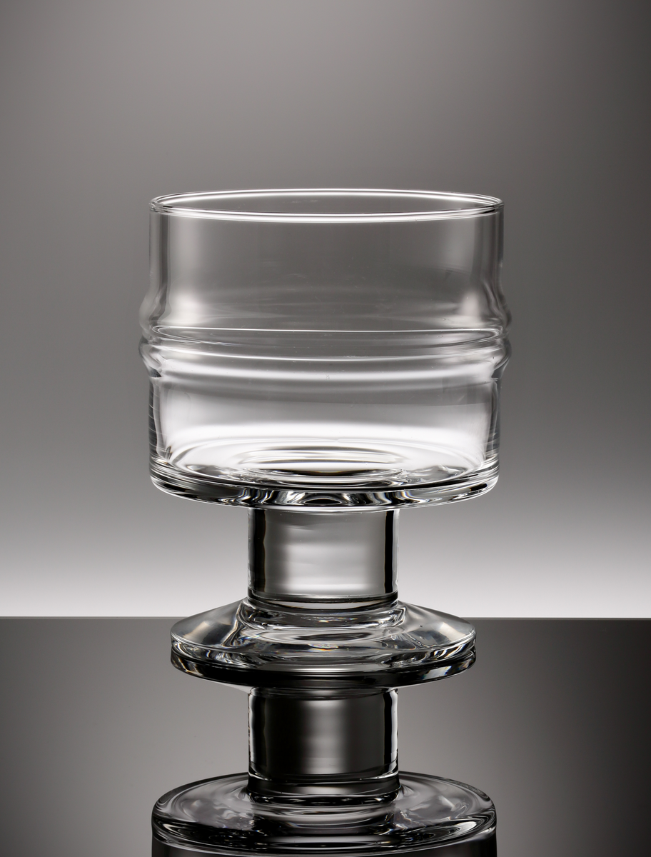 "Droppring", formgiven av Timo Sarpaneva för Iittala glasbruk. Vitvinsglas på ben och fot. Cylindrisk skål, med två vulster på livet. Kort och bastant ben.