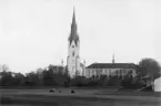 Utblick över den gamla kreatursvallen mot Linköpings mest betecknande byggnader. Fotoögonblicket dateras till omkring sekelskiftet 1900 och domkyrkan var då i sin nya skepnad dryga tio år gammal. Även slottet hade under 1800-talet genomgått stor förändring. Under seklets mer romantiska period hade man velat återskapa byggnaden som ett historiskt renässansslott med loftgång och praktgavlar. Det mesta av förändringarna återspeglades dock på slottets fasad mot öster, mot stadens centrala delar. En intressant detalj i bilden ses i bildens nedre, högra hörn. Där får vi en skymt av Linköpings ridhus som sällan återgivits. Ridhuset var uppfört 1885 och drevs vid tiden som aktiebolag.