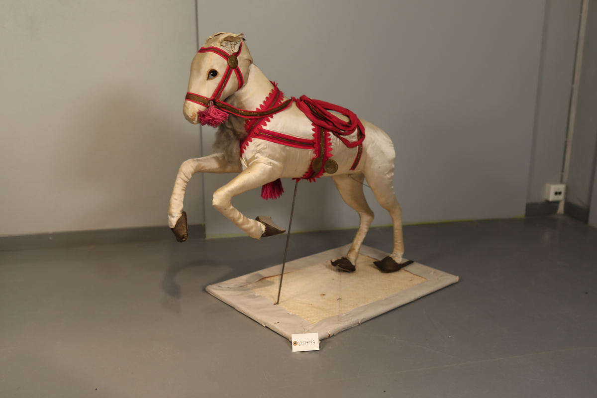 Utstillingsfigur montert på plate. Figuren er utformet som et reinsdyr i hvitt, silkeaktig stoff med brune klover og filtøyne. Geviret er surret inn med gullbånd og har sokler til lyspærer i taggene. Geviret er avtagbart. Reinsdyret har seletøy i rosa og lilla filt med gulltråd og runde metallplater. Juletrelysene til geviret er Philips 14v. Det stikker ender av ledninger ut av både kroppen og geviret. 

Reinsdyret består av flere deler:
a - kropp montert på plate med metallstøtte foran og bena skrudd fast bak. På et tidspunkt har noen stiftet fast papir over ytterkantene av det originalet stoffet.
b - gevir med plass til 8 lyspærer
c - gevir med plass til 7 lyspærer
d - løs pyntedusk
e - grå ledning
f til u - 16 lyspærer