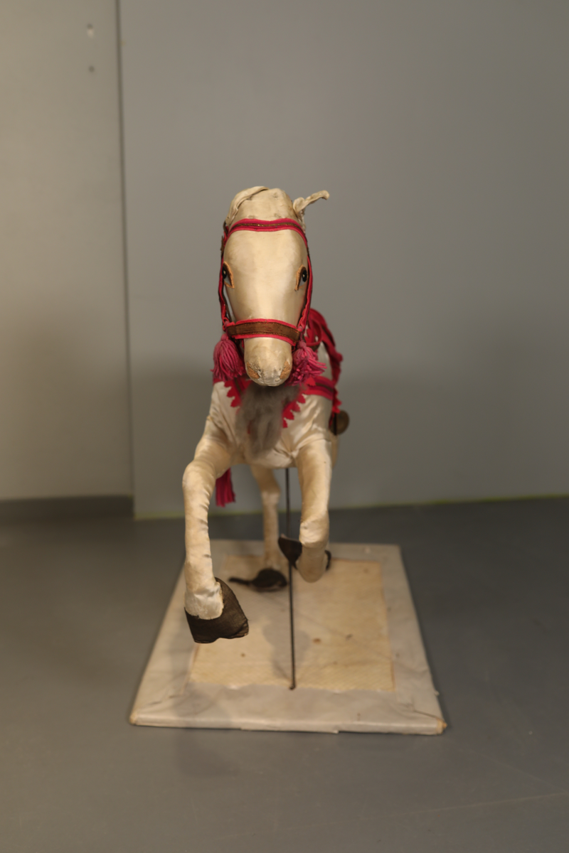 Utstillingsfigur montert på plate. Figuren er utformet som et reinsdyr i hvitt, silkeaktig stoff med brune klover og filtøyne. Geviret er surret inn med gullbånd og har sokler til lyspærer i taggene. Geviret er avtagbart. Reinsdyret har seletøy i rosa og lilla filt med gulltråd og runde metallplater. Juletrelysene til geviret er Philips 14v. Det stikker ender av ledninger ut av både kroppen og geviret. 

Reinsdyret består av flere deler:
a - kropp montert på plate med metallstøtte foran og bena skrudd fast bak. På et tidspunkt har noen stiftet fast papir over ytterkantene av det originalet stoffet.
b - gevir med plass til 8 lyspærer
c - gevir med plass til 7 lyspærer
d - løs pyntedusk
e - grå ledning
f til u - 16 lyspærer