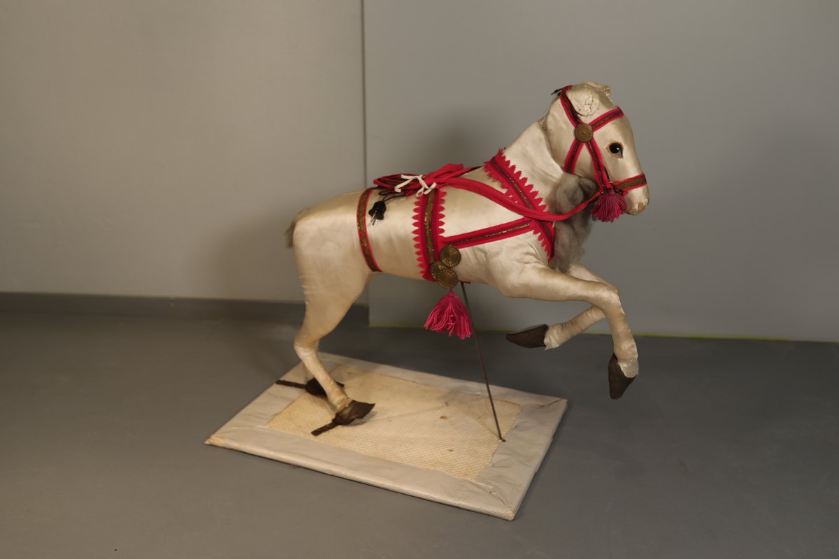 Utstillingsfigur montert på plate. Figuren er utformet som et reinsdyr i hvitt, silkeaktig stoff med brune klover og filtøyne. Geviret er surret inn med gullbånd og har sokler til lyspærer i taggene. Geviret er avtagbart. Reinsdyret har seletøy i rosa og lilla filt med gulltråd og runde metallplater. Juletrelysene til geviret er Philips 14v. Det stikker ender av ledninger ut av både kroppen og geviret. 

Reinsdyret består av flere deler:
a - kropp montert på plate med metallstøtte foran og bena skrudd fast bak. På et tidspunkt har noen stiftet fast papir over ytterkantene av det originalet stoffet.
b - gevir med plass til 8 lyspærer
c - gevir med plass til 7 lyspærer
d - løs pyntedusk
e - grå ledning
f til u - 16 lyspærer