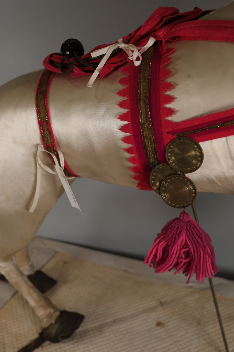 Utstillingsfigur montert på plate. Figuren er utformet som et reinsdyr i hvitt, silkeaktig stoff med brune klover og filtøyne. Geviret er surret inn med gullbånd og har sokler til lyspærer i taggene. Geviret er avtagbart. Reinsdyret har seletøy i rosa og lilla filt med gulltråd og runde metallplater. Juletrelysene til geviret er Philips 14v. Det stikker ender av ledninger ut av både kroppen og geviret. 

Reinsdyret består av flere deler:
a - kropp montert på plate med metallstøtte foran og bena skrudd fast bak. På et tidspunkt har noen stiftet fast papir over ytterkantene av det originalet stoffet.
b - gevir med plass til 8 lyspærer
c - gevir med plass til 7 lyspærer
d - løs pyntedusk
e - grå ledning
f til u - 16 lyspærer