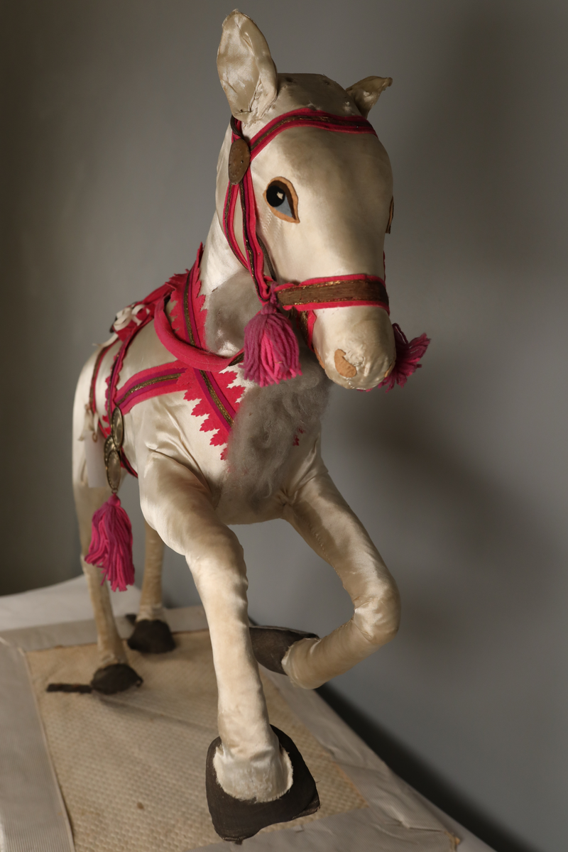 Utstillingsfigur montert på plate. Figuren er utformet som et reinsdyr i hvitt, silkeaktig stoff med brune klover og filtøyne. Geviret er surret inn med gullbånd og har sokler til lyspærer i taggene. Geviret er avtagbart. Reinsdyret har seletøy i rosa og lilla filt med gulltråd og runde metallplater. Juletrelysene til geviret er Philips 14v. Det stikker ender av ledninger ut av både kroppen og geviret. 

Reinsdyret består av flere deler:
a - kropp montert på plate med metallstøtte foran og bena skrudd fast bak. På et tidspunkt har noen stiftet fast papir over ytterkantene av det originalet stoffet.
b - gevir med plass til 8 lyspærer
c - gevir med plass til 7 lyspærer
d - løs pyntedusk
e - grå ledning
f til u - 16 lyspærer