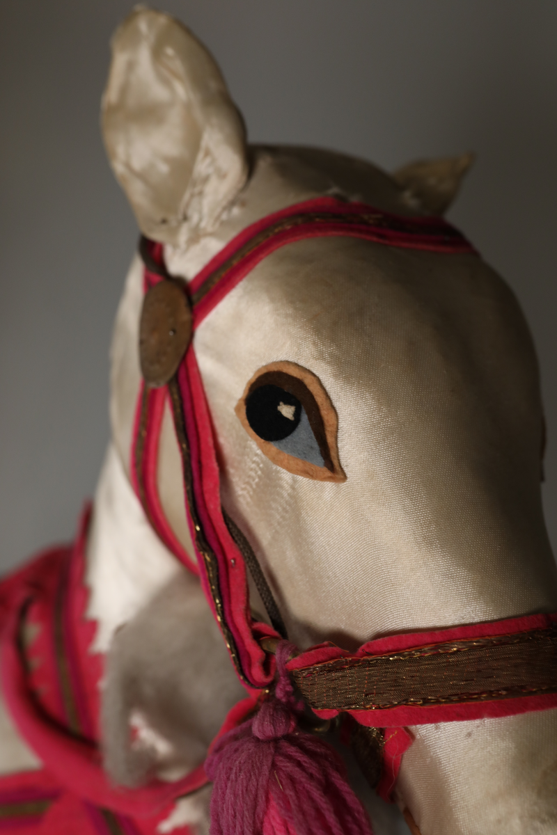 Utstillingsfigur montert på plate. Figuren er utformet som et reinsdyr i hvitt, silkeaktig stoff med brune klover og filtøyne. Geviret er surret inn med gullbånd og har sokler til lyspærer i taggene. Geviret er avtagbart. Reinsdyret har seletøy i rosa og lilla filt med gulltråd og runde metallplater. Juletrelysene til geviret er Philips 14v. Det stikker ender av ledninger ut av både kroppen og geviret. 

Reinsdyret består av flere deler:
a - kropp montert på plate med metallstøtte foran og bena skrudd fast bak. På et tidspunkt har noen stiftet fast papir over ytterkantene av det originalet stoffet.
b - gevir med plass til 8 lyspærer
c - gevir med plass til 7 lyspærer
d - løs pyntedusk
e - grå ledning
f til u - 16 lyspærer