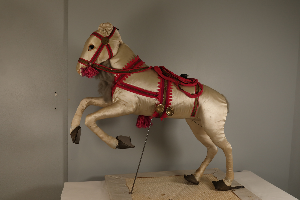 Utstillingsfigur montert på plate. Figuren er utformet som et reinsdyr i hvitt, silkeaktig stoff med brune klover og filtøyne. Geviret er surret inn med gullbånd og har sokler til lyspærer i taggene. Geviret er avtagbart. Reinsdyret har seletøy i rosa og lilla filt med gulltråd og runde metallplater. Juletrelysene til geviret er Philips 14v. Det stikker ender av ledninger ut av både kroppen og geviret. 

Reinsdyret består av flere deler:
a - kropp montert på plate med metallstøtte foran og bena skrudd fast bak. På et tidspunkt har noen stiftet fast papir over ytterkantene av det originalet stoffet.
b - gevir med plass til 8 lyspærer
c - gevir med plass til 7 lyspærer
d - løs pyntedusk
e - grå ledning
f til u - 16 lyspærer