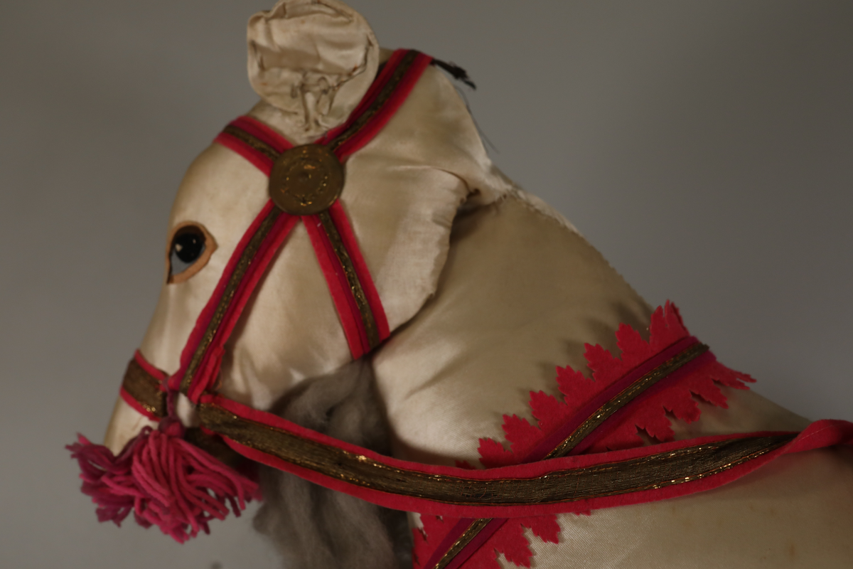 Utstillingsfigur montert på plate. Figuren er utformet som et reinsdyr i hvitt, silkeaktig stoff med brune klover og filtøyne. Geviret er surret inn med gullbånd og har sokler til lyspærer i taggene. Geviret er avtagbart. Reinsdyret har seletøy i rosa og lilla filt med gulltråd og runde metallplater. Juletrelysene til geviret er Philips 14v. Det stikker ender av ledninger ut av både kroppen og geviret. 

Reinsdyret består av flere deler:
a - kropp montert på plate med metallstøtte foran og bena skrudd fast bak. På et tidspunkt har noen stiftet fast papir over ytterkantene av det originalet stoffet.
b - gevir med plass til 8 lyspærer
c - gevir med plass til 7 lyspærer
d - løs pyntedusk
e - grå ledning
f til u - 16 lyspærer