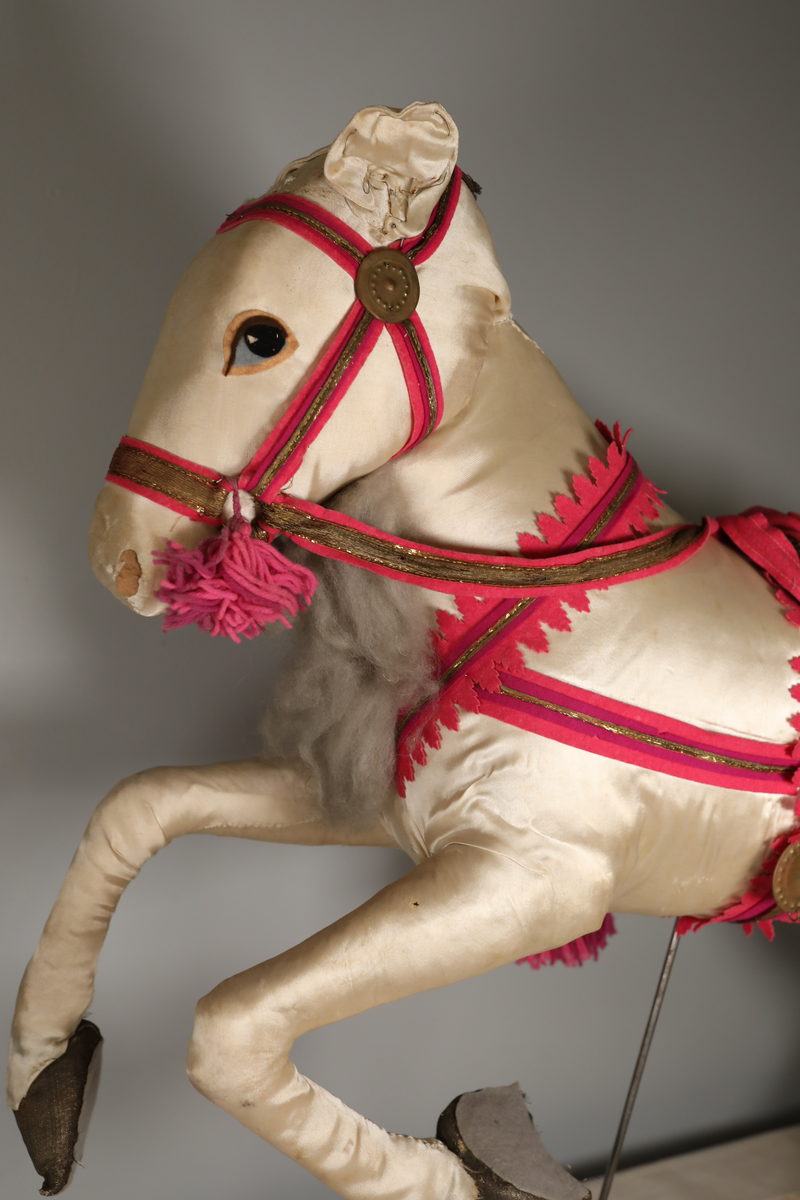 Utstillingsfigur montert på plate. Figuren er utformet som et reinsdyr i hvitt, silkeaktig stoff med brune klover og filtøyne. Geviret er surret inn med gullbånd og har sokler til lyspærer i taggene. Geviret er avtagbart. Reinsdyret har seletøy i rosa og lilla filt med gulltråd og runde metallplater. Juletrelysene til geviret er Philips 14v. Det stikker ender av ledninger ut av både kroppen og geviret. 

Reinsdyret består av flere deler:
a - kropp montert på plate med metallstøtte foran og bena skrudd fast bak. På et tidspunkt har noen stiftet fast papir over ytterkantene av det originalet stoffet.
b - gevir med plass til 8 lyspærer
c - gevir med plass til 7 lyspærer
d - løs pyntedusk
e - grå ledning
f til u - 16 lyspærer