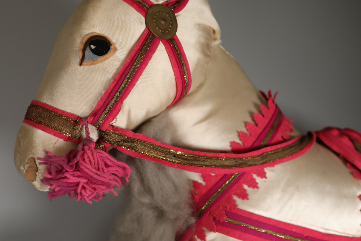 Utstillingsfigur montert på plate. Figuren er utformet som et reinsdyr i hvitt, silkeaktig stoff med brune klover og filtøyne. Geviret er surret inn med gullbånd og har sokler til lyspærer i taggene. Geviret er avtagbart. Reinsdyret har seletøy i rosa og lilla filt med gulltråd og runde metallplater. Juletrelysene til geviret er Philips 14v. Det stikker ender av ledninger ut av både kroppen og geviret. 

Reinsdyret består av flere deler:
a - kropp montert på plate med metallstøtte foran og bena skrudd fast bak. På et tidspunkt har noen stiftet fast papir over ytterkantene av det originalet stoffet.
b - gevir med plass til 8 lyspærer
c - gevir med plass til 7 lyspærer
d - løs pyntedusk
e - grå ledning
f til u - 16 lyspærer