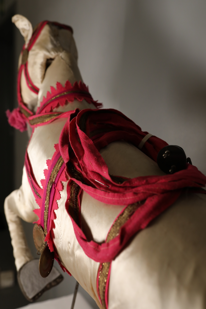 Utstillingsfigur montert på plate. Figuren er utformet som et reinsdyr i hvitt, silkeaktig stoff med brune klover og filtøyne. Geviret er surret inn med gullbånd og har sokler til lyspærer i taggene. Geviret er avtagbart. Reinsdyret har seletøy i rosa og lilla filt med gulltråd og runde metallplater. Juletrelysene til geviret er Philips 14v. Det stikker ender av ledninger ut av både kroppen og geviret. 

Reinsdyret består av flere deler:
a - kropp montert på plate med metallstøtte foran og bena skrudd fast bak. På et tidspunkt har noen stiftet fast papir over ytterkantene av det originalet stoffet.
b - gevir med plass til 8 lyspærer
c - gevir med plass til 7 lyspærer
d - løs pyntedusk
e - grå ledning
f til u - 16 lyspærer