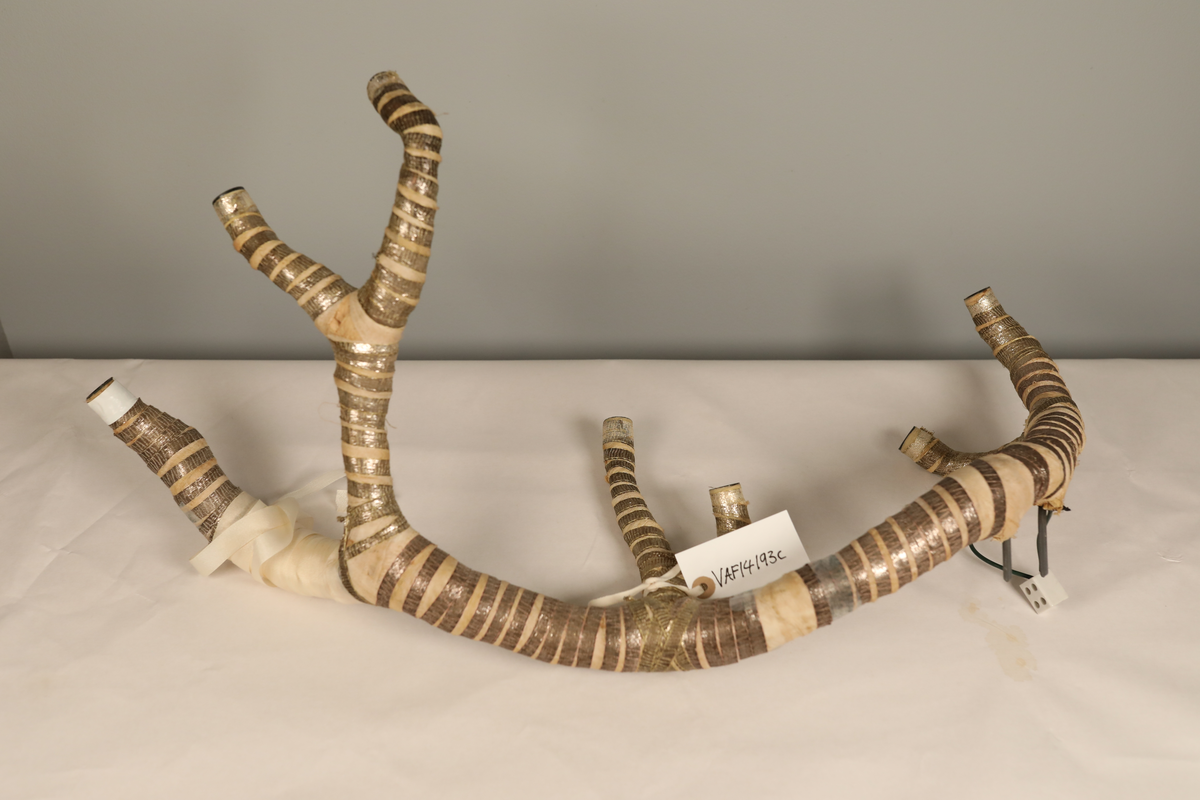 Utstillingsfigur montert på plate. Figuren er utformet som et reinsdyr i hvitt, silkeaktig stoff med brune klover og filtøyne. Geviret er surret inn med gullbånd og har sokler til lyspærer i taggene. Geviret er avtagbart. Reinsdyret har seletøy i rosa og lilla filt med gulltråd og runde metallplater. Juletrelysene til geviret er Philips 14v. Det stikker ender av ledninger ut av både kroppen og geviret. 

Reinsdyret består av flere deler:
a - kropp montert på plate med metallstøtte foran og bena skrudd fast bak. På et tidspunkt har noen stiftet fast papir over ytterkantene av det originalet stoffet.
b - gevir med plass til 8 lyspærer
c - gevir med plass til 7 lyspærer
d - løs pyntedusk
e - grå ledning
f til u - 16 lyspærer