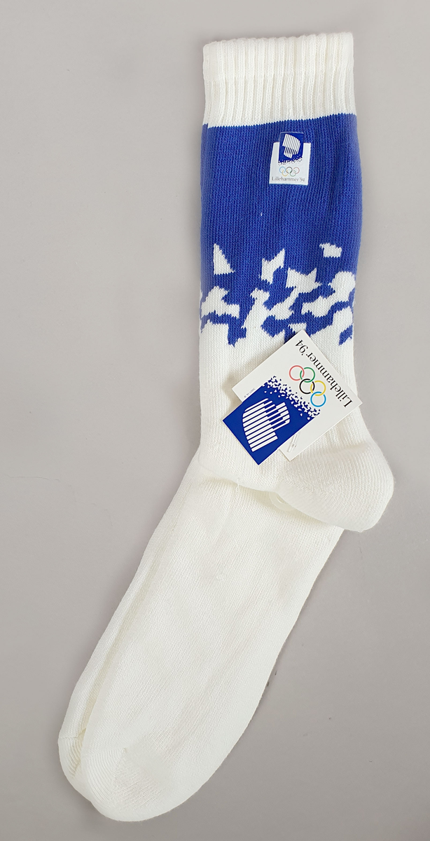 Hvite sokker av bomullsfrotté med krystallmønster i blått og tekstilmerke med logo for Lillehammer '94 .