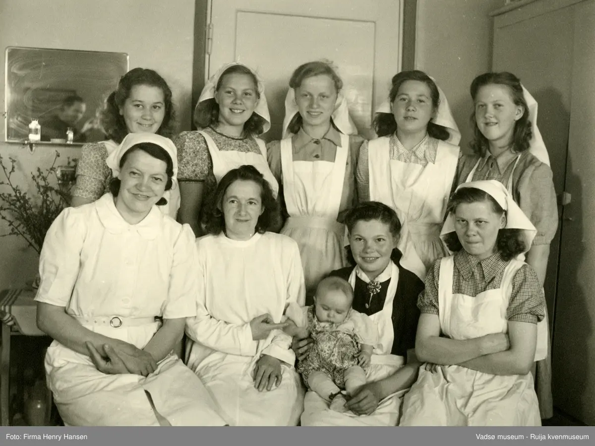 Sanitetsforeningens Fødehjem, Vadsø. En del av sanitetsforeningens personale og en baby. Jordmor  Elisabeth Pedersen nr 2 fra venstre og Elisabeth Methi nr 3 fra venstre i andre rekke. I Vadsø  bygde sanitetsforeningen et stort fødehjem med legekontor og kontrollstasjon for mor og barn. Fødehjemmet ble bygd i 1952, arkitekt Finn Eidvin  og hovedentreprenør Alrik Basma. Fødehjemmet ble lagt ned i  1966.
Kilde: Trond M.E.Dancke "Opp av ruinene, Gjenreisning av Finnmark 1945-1960."