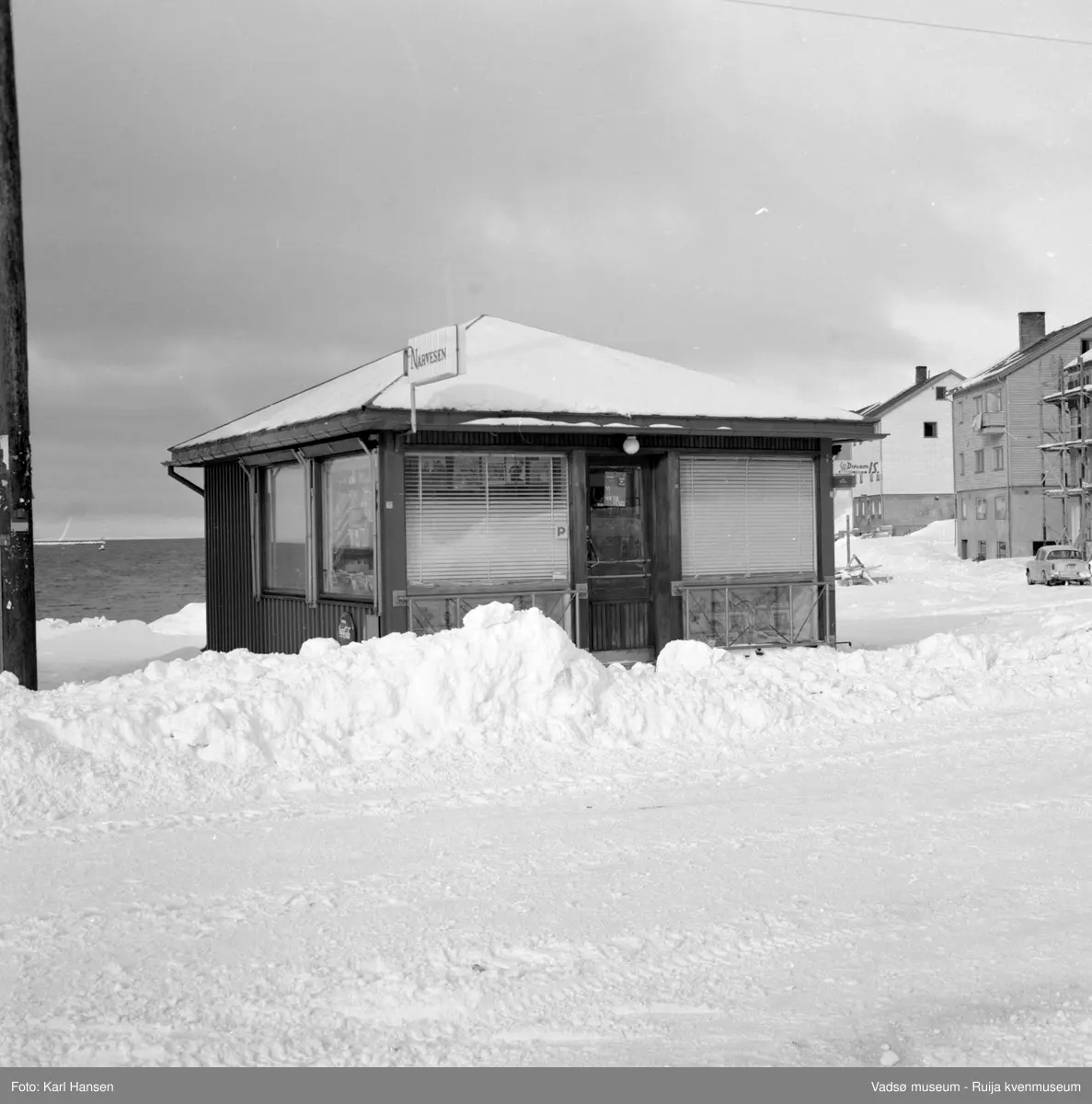 Narvesenkiosken Tollbugata i Vadsø, en vinterdag. Bildet er tatt mot vest og  i bakgrunn ser vi havna og deler av Kaigata.