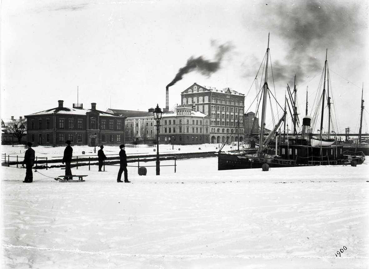 Vy över Tullhamnen med Tullhuset och Ångkvarnen vintern 1900. I förgrunden fyra "statister" varav en med kälke. Till höger Herman Sandbergs son. Vid kajen ligger ångbåten Kalmar. 
Reprofoto.