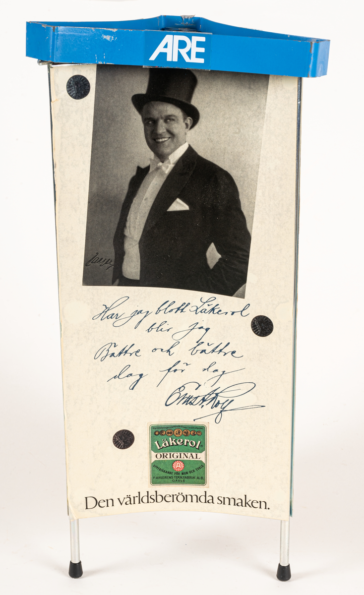 Reklamskylt, reklampelare på tre ben med plastfötter, i metall och papp, för Läkerol. Intygsreklam med citat från tre kändisar: Joséphine Baker, Ernst Rolf och Maurice Chevalier på de tre sidorna.