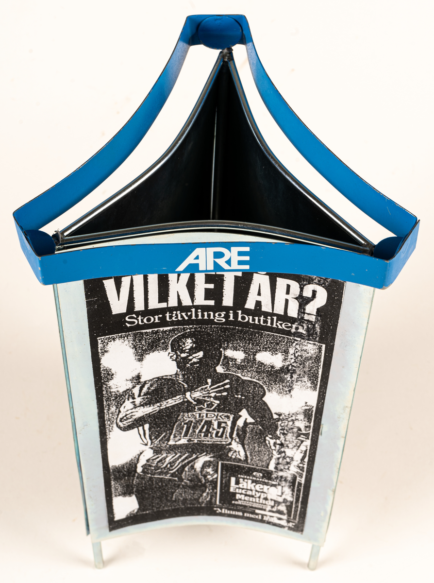 Reklamskylt, reklampelare på tre ben, i metall och papp, för Läkerol. Tre olika bilder i svart-vitt med kändisar: VILKET ÅR? Stor tävleing i butiken. 
Bilderna föreställer Ingemar Johansson "Ingo", ABBA och eventuellt Bob Hayes.