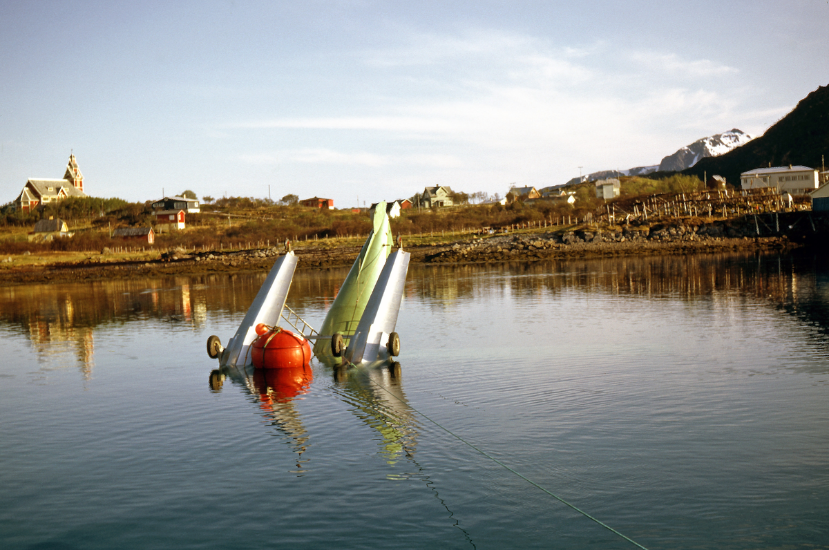Widerøes DHC-3 Otter, LN-SUV, har blitt sikret etter havari ved Gravdal  i Lofoten. Det er montert hjul på flottørene for å kunne ta flyet opp på land. Buksnes kirke i bakgrunnen.