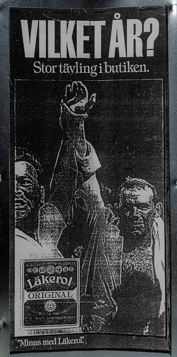 Reklamskylt, reklampelare på tre ben, i metall och papp, för Läkerol. Tre olika bilder i svart-vitt med kändisar: VILKET ÅR? Stor tävleing i butiken. 
Bilderna föreställer Ingemar Johansson "Ingo", ABBA och eventuellt Bob Hayes.