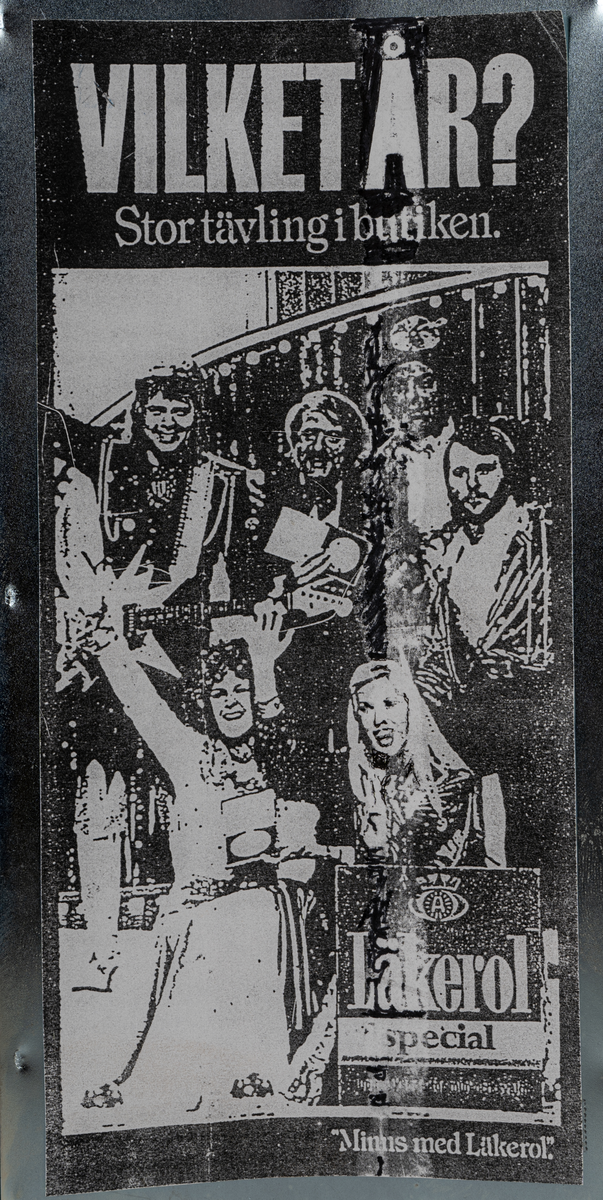 Reklamskylt, reklampelare på tre ben, i metall och papp, för Läkerol. Tre olika bilder i svart-vitt med kändisar: VILKET ÅR? Stor tävleing i butiken. 
Bilderna föreställer Ingemar Johansson "Ingo", ABBA och eventuellt Bob Hayes.