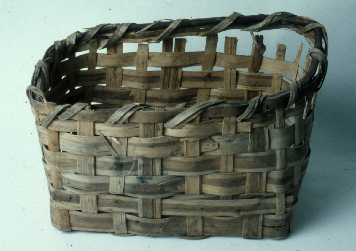 Korg i rakflätad spån. Kantens vidja är lindad. Rektangulär form med flätad botten.
