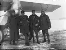 Gruppfoto av fyra militärer från Österrike-Ungern ståendes vid nosen ett flygplan under första världskriget. Vintertid. Längst till höger Edmund Sparmann i flygarhuva.