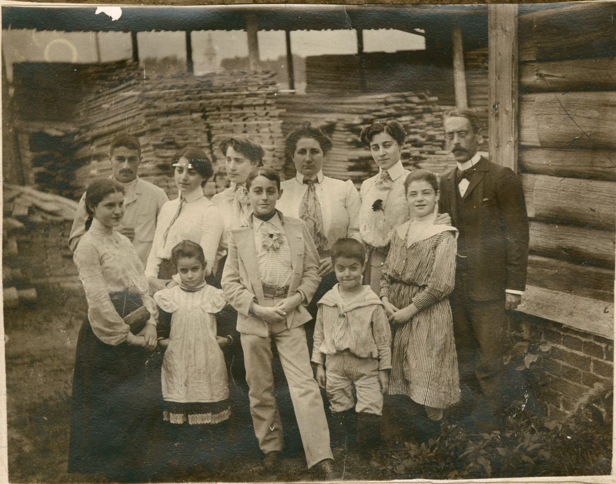 Motivet viser familien Rostin samlet for fotografering foran en tømmerbygning. Trolig teglsteinfabrikken i Borovitsji. Foran fra venstre: Julia, Serafima, Ignazy, Nicolay, Victoria. Bak fra venstre: Theodor, Elisabeth, Valentine, Sonja, Florentine, ukjent mann.