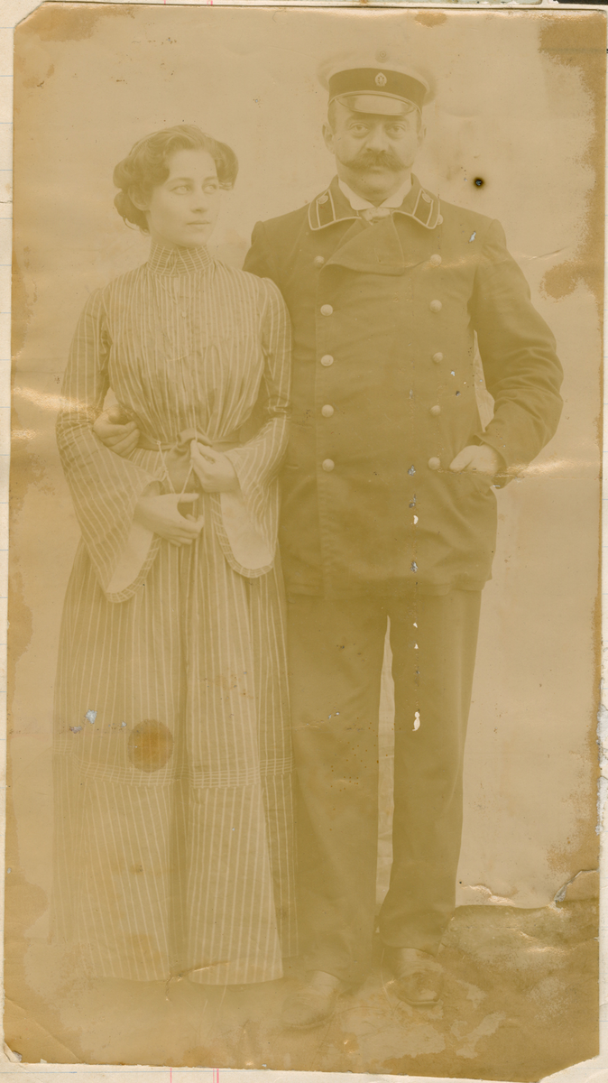 Florentine Rostin og hennes onkel, Helidor Rostin, poserer sammen. Helidor er uniformert og Florentine er ikledd en stripete kjole med vide ermer og et langt kroppssmykke som hun hviler tommelen i.