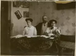 Søsknene Valentine og Florentine avbildet sammen med sin far, Mikhail Rostin, som holder døtrene på skuldrene. De sitter på en divan med et mønstret sengeteppe. På den tapetserte veggen bak henger et maleri og en krydderhylle. Bordet er dekket av en fløyelsduk og aviser.
