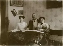 Søsknene Valentine og Florentine avbildet sammen med sin far, Mikhail Rostin. Mikhail holder Florentine på skulderen. De sitter på en divan med et mønstret sengeteppe og leser aviser. På den tapetserte veggen bak henger et maleri og en krydderhylle. Bordet har en mørk fløyelsduk.