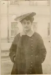 Motivet viser en Elisabeth Rostin fotografert utendørs på gaten foran en bygning. Hun er ikledd en hatt med blondedetaljer og en romslig kåpe med knapper og lys krage. Hun står med hendene i lomma.