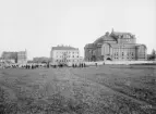 Ett fruset ögonblick från Linköping 1903. Vy från det sedermera utlagda Vasatorget med blicken vänd rakt österut. Vid tiden var som synes ännu inte heller Vasavägen utlagd i området. En idé som snart skulle bli en verklighet var dock stadens nya teater. Här ser vi teaterbyggnaden till fullo rest men ännu i avsaknad av sin gulmenade puts. Från vänster ser vi för Linköpingsbor välbekanta byggnader i Miljonpalatset, i fonden Överstehuset med grannfastighet och invid teatern Brandstodsbolagets vid tiden helt nyligen färdigställda kontor. Övrigt att notera i bilden är att stadens sanitetsproblem nu tagits på allvar och att stora resurser nedlades på funktionella avloppssystem.