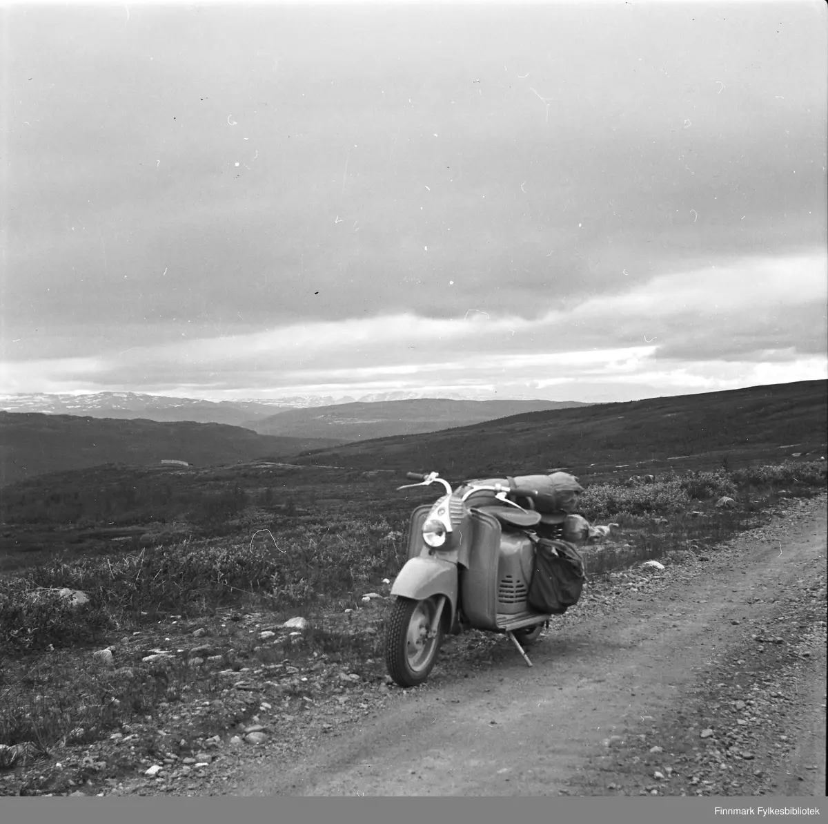 Scooterferie 1955 i Beaskáđas. Scooteren er av det østerrikske merket Puch. Beaskáđas er et fjellområde på grensen mellom kommunene Alta og Kautokeino, et fjelldrag i utkanten av Finnmarksvidda.