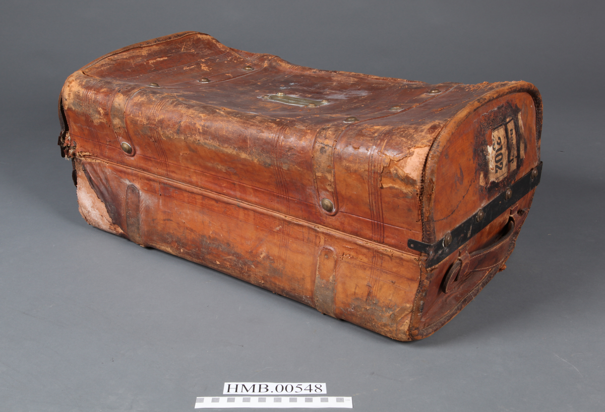 Rektangulær koffert med avrundede hjørner. To utvendige låser og to remmer med spenne. Fõret. Innvendig stor lomme i lokket.