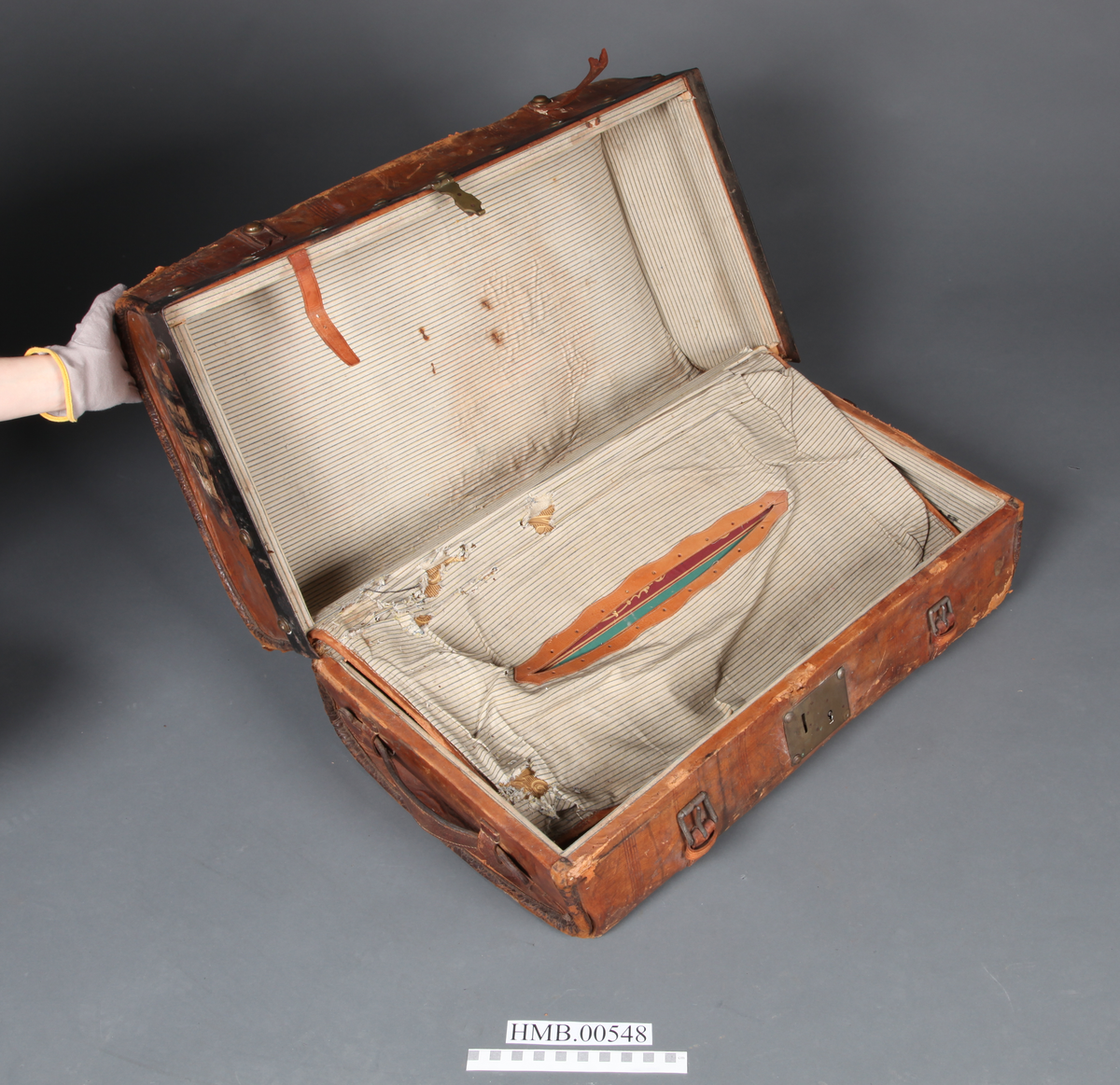 Rektangulær koffert med avrundede hjørner. To utvendige låser og to remmer med spenne. Fõret. Innvendig stor lomme i lokket.